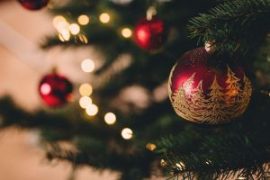 Close-up of a decorated Christmas tree with red ornaments and warm, glowing lights, featuring a beautifully painted bauble with trees.
