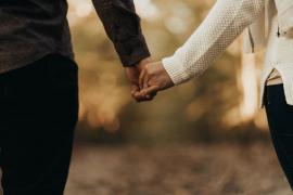 A close-up of a couple's hands intertwined, with one wearing a textured white sweater and the other in a dark button-up shirt.