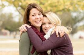Two women embrace joyfully outdoors, surrounded by soft autumn leaves, conveying warmth and a strong friendship.