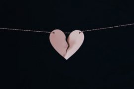 A pink, broken heart hanging on a string against a dark background, symbolizing separation or lost love.