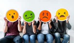 Four people sitting on a couch hold large emoji faces, expressing various emotions: happiness, disgust, anger, and sadness.