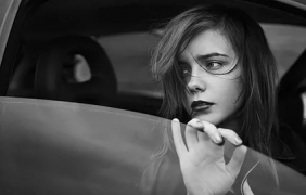 A person extends their hand through a car window, set against a blurred background in black and white.