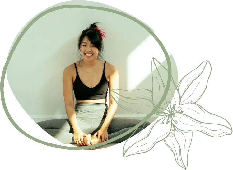 A person sits cross-legged on the floor, wearing a black sports top and gray leggings, with a light background and decorative floral overlay.