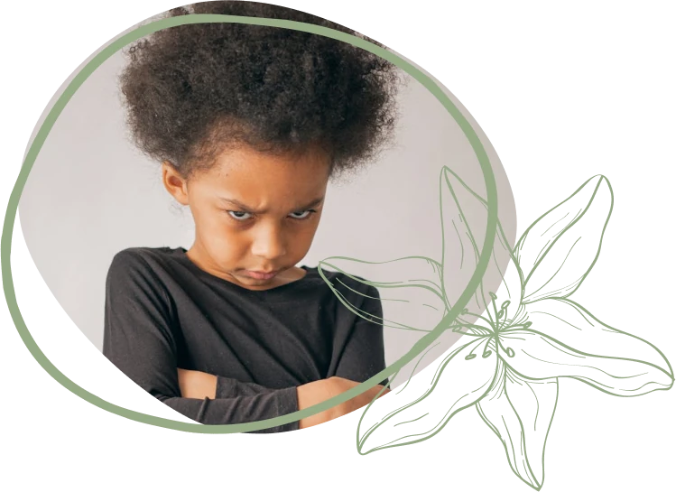 A child with a large, fluffy hairstyle wears a black long-sleeve shirt, crossed arms, against a light gray backdrop with floral design.