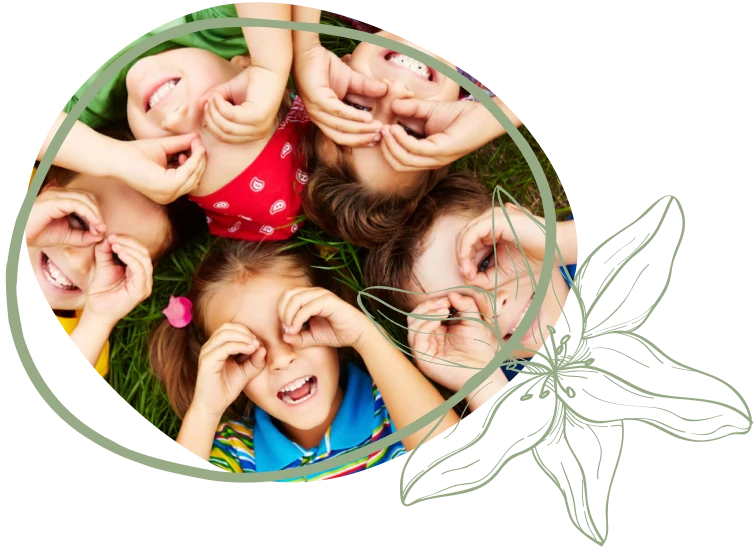 A group of children lying in a circle on grass, smiling and making playful faces with their hands. Vibrant clothing adds to the joyful scene.