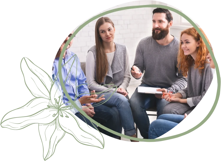 A group of people in casual attire engaged in a discussion, seated in a circle with notes in hand, against a soft, neutral background.