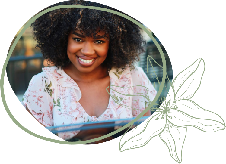 A person with curly hair wears a floral blouse, seated at a table with decorative elements and a hand resting on the edge.