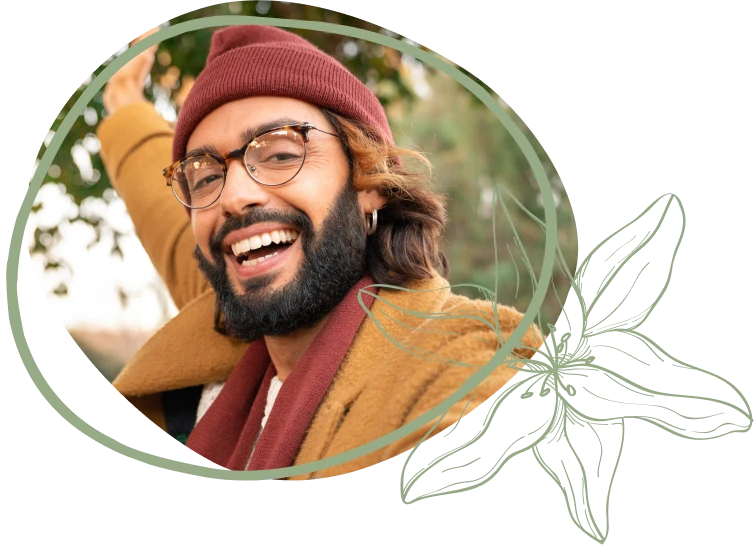 A person in a cozy brown coat and maroon beanie gestures joyfully outdoors, surrounded by greenery and floral motifs.