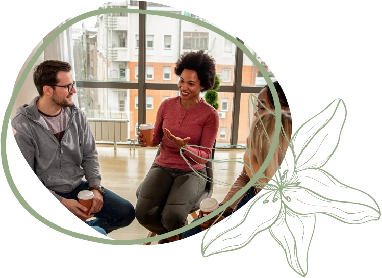 A group of three people engaged in a conversation while holding coffee cups, set in a modern, sunlit room with large windows.