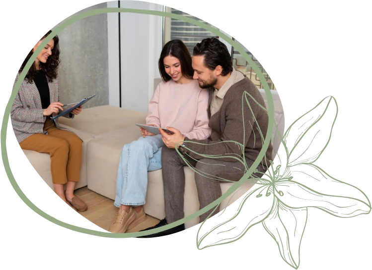 A woman and a man are seated on a light-colored sofa, interacting with a digital device together. Another woman is nearby, looking at her tablet.
